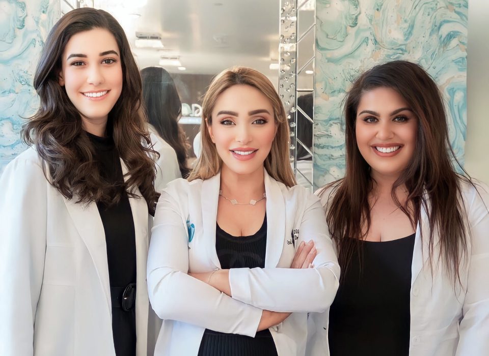 Three dentist in white lab coats stand together, smiling.