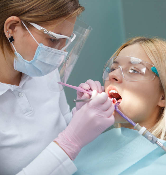 Dental hygienist performing oral exam on a patient wearing protective eyewear and a mask.