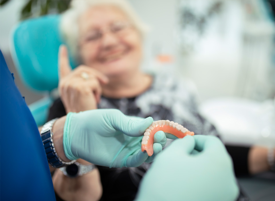 Dental professional showing a set of dentures to a smiling senior patient.