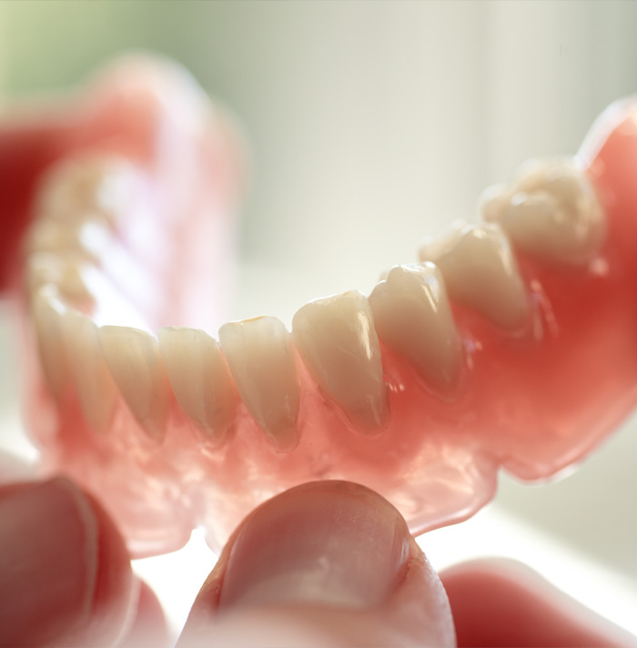 Partial dentures held in a hand, showing teeth and gumline.