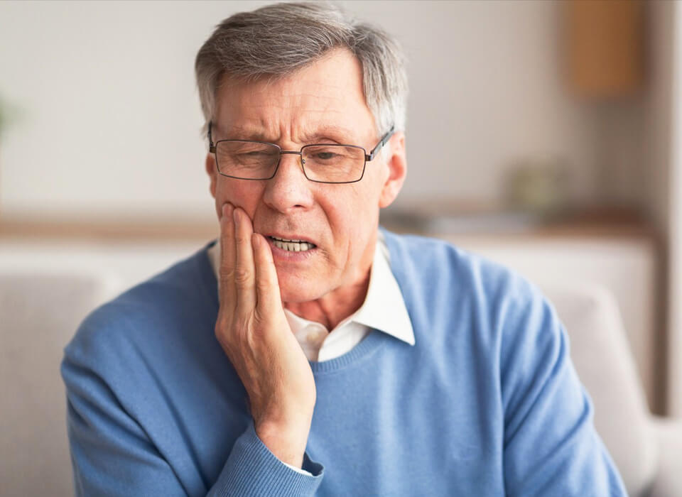 Senior man holding his cheek, appearing distressed and experiencing dental pain.