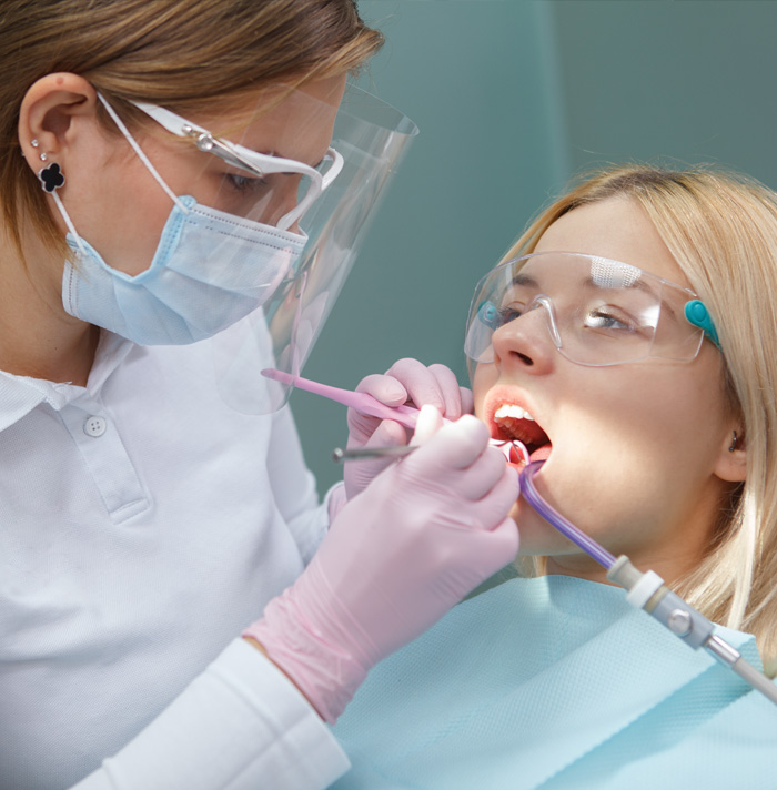 Dental hygienist performing oral exam on a patient wearing protective eyewear and a mask.