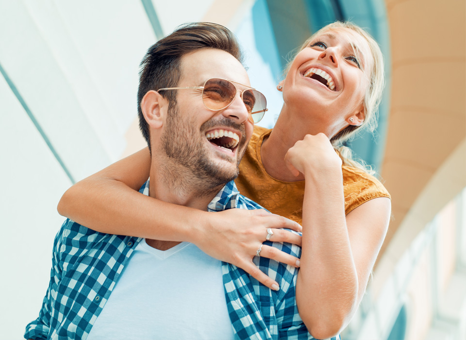 Happy couple laughing while woman embracing man's shoulders in an outdoor setting.