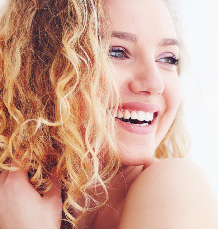 Close-up of a woman with curly blonde hair, smiling broadly, showcasing a bright white smile.