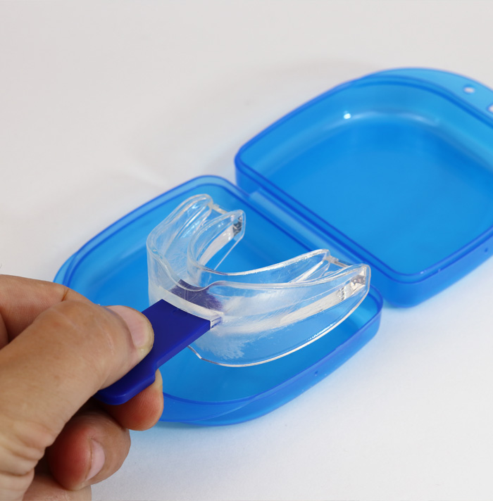 Clear plastic mouthguard in a blue carrying case, held by a hand.