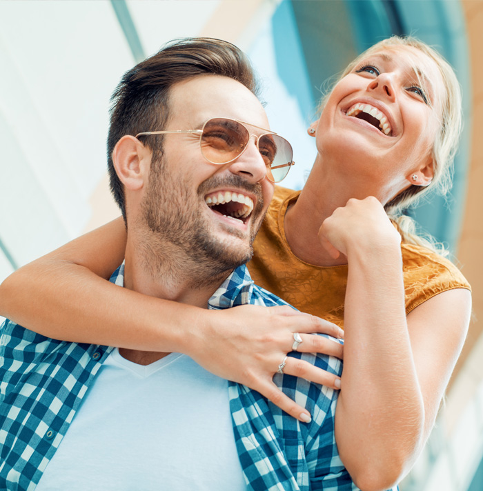 Happy couple laughing while woman embracing man's shoulders in an outdoor setting.