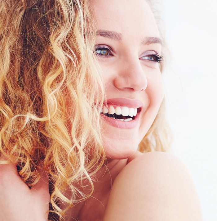 Close-up of a woman with curly blonde hair, smiling broadly, showcasing a bright white smile.