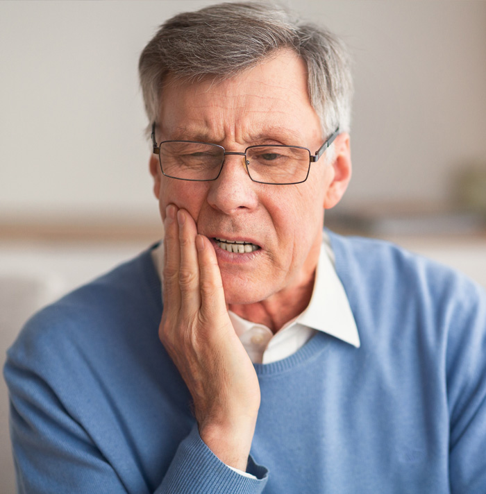 Senior man holding his cheek, appearing distressed and experiencing dental pain.